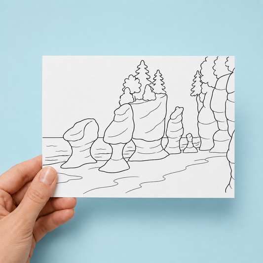 Hand holding a black-and-white colouring greeting card illustrated with the Hopewell Rocks flowerpot rock formations along the Bay of Fundy shoreline, with trees on top of the rocks, against a light blue background.