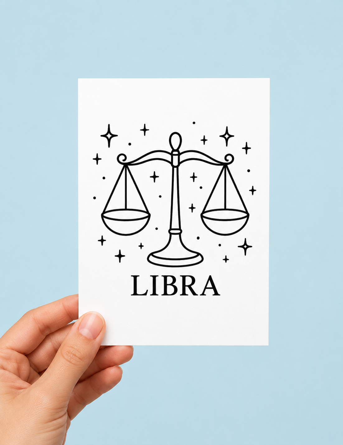 A hand holding a white card featuring a black line art illustration of a Libra zodiac sign, including the scales of justice and the word 'LIBRA', against a solid light blue background.