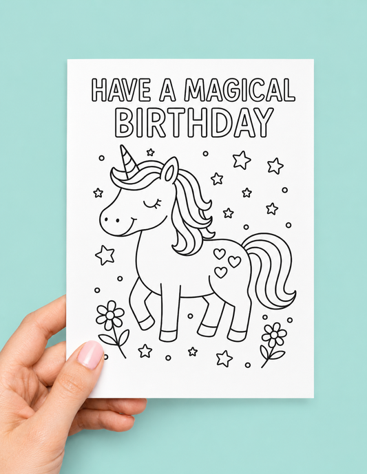 A hand holds a white greeting card with black line art of a unicorn and the text 'HAVE A MAGICAL BIRTHDAY' against a light aqua background.